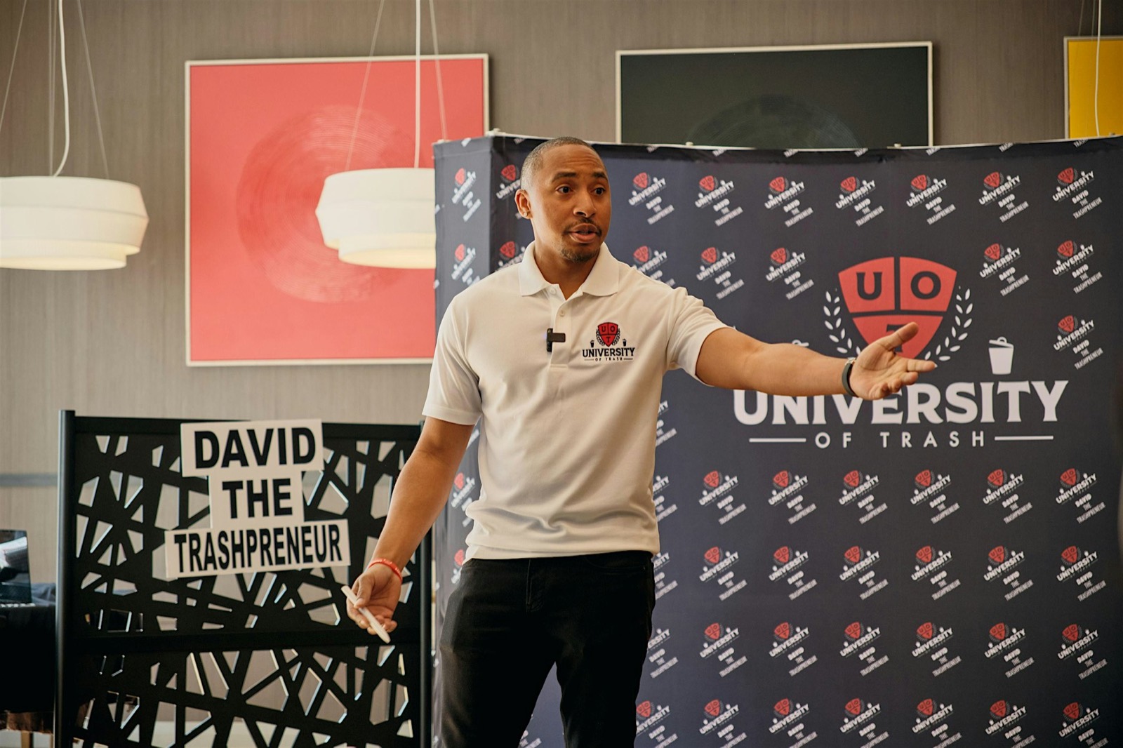 David Simes training a room in a University of Trash polo in front of a branded UOT step-and-repeat backdrop.